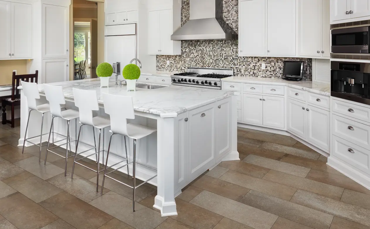 mosiac glass tile backsplash in kitchen with white cabinets, marble countertop and tile flooring